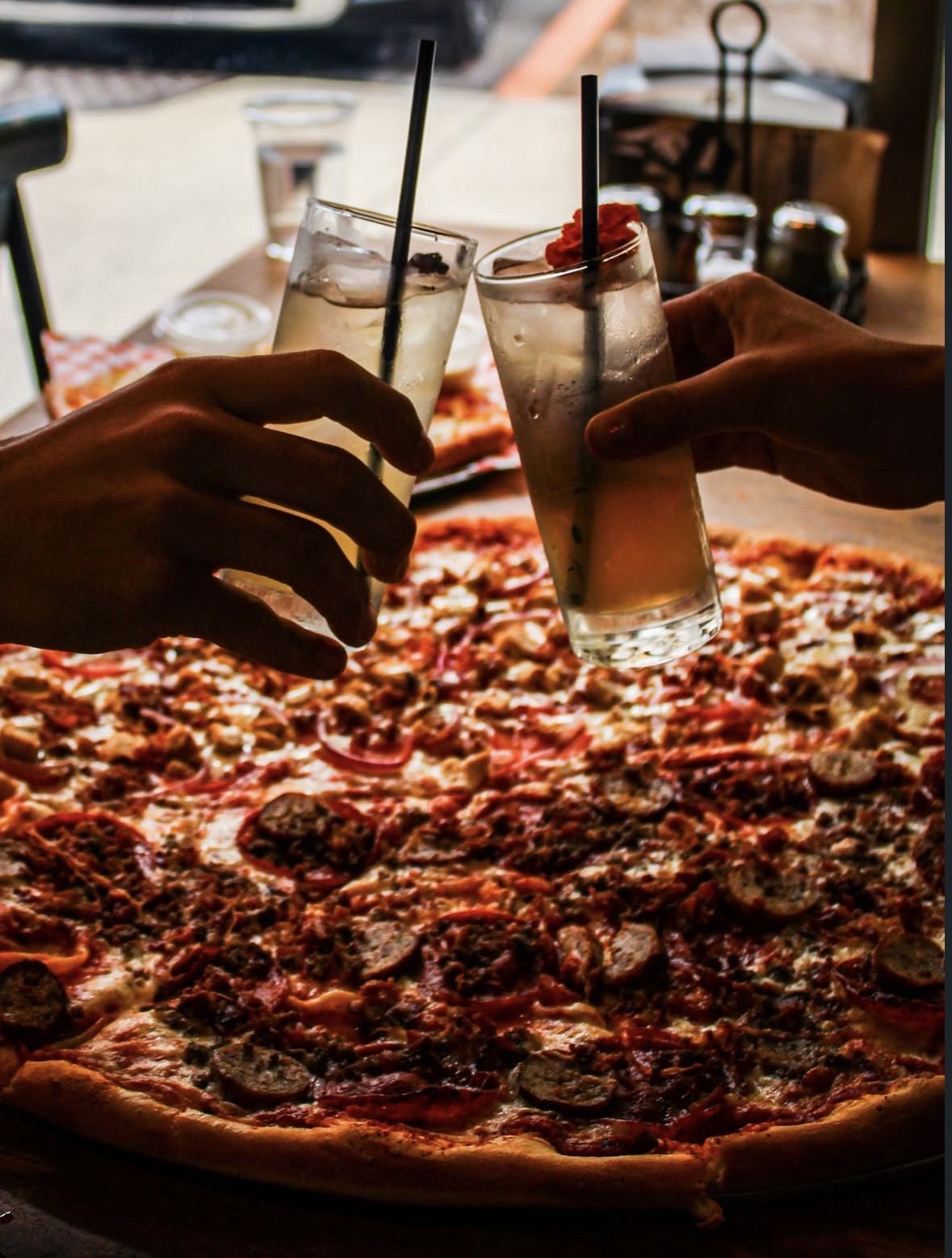 Two drinks clinking over a 22-inch pie at Goodfellas Pizzeria, Indianapolis